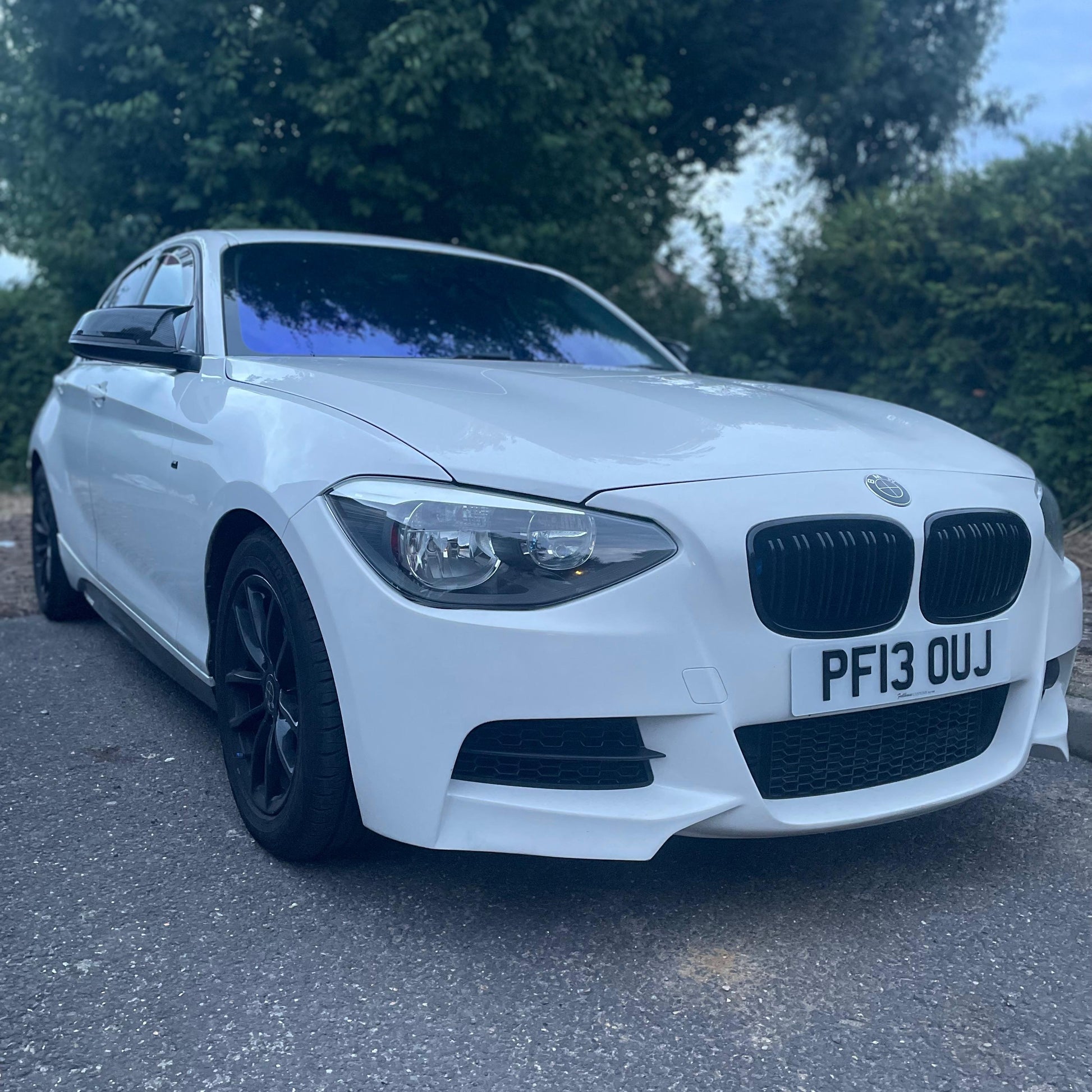 White BMW car parked on a road with greenery in the background
